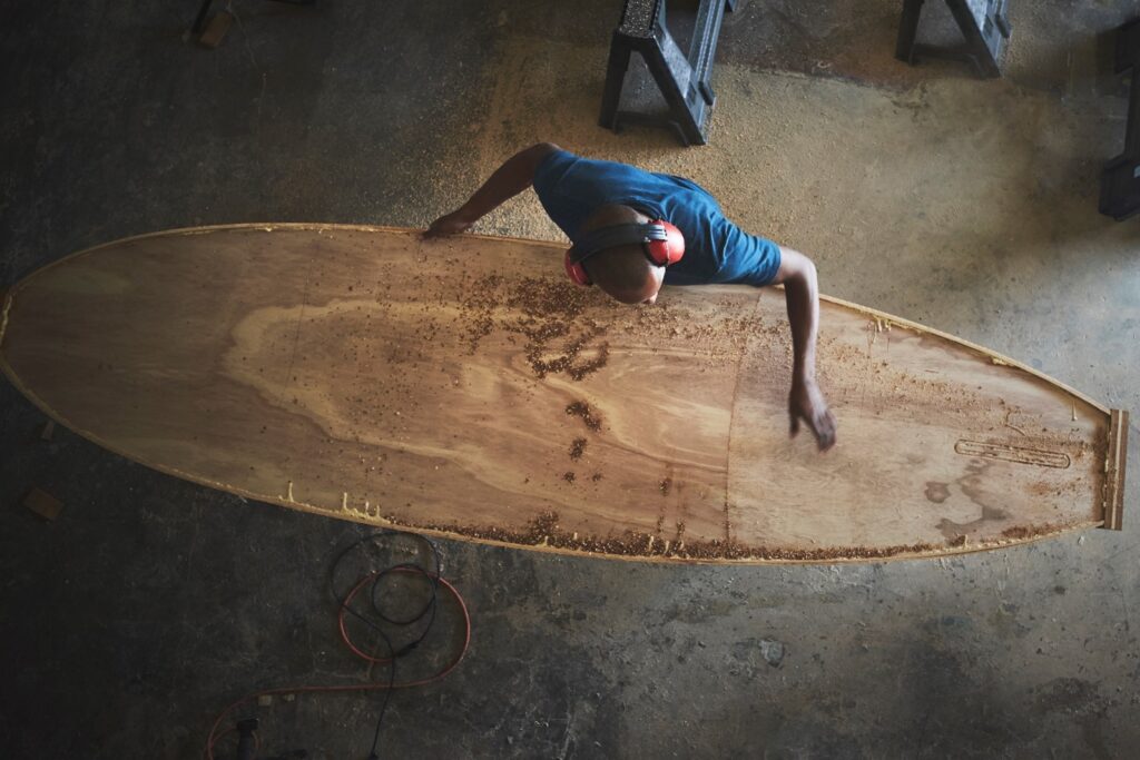 man finishing timber surfboard